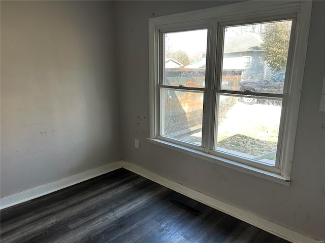 spare room with plenty of natural light, baseboards, visible vents, and dark wood-style flooring