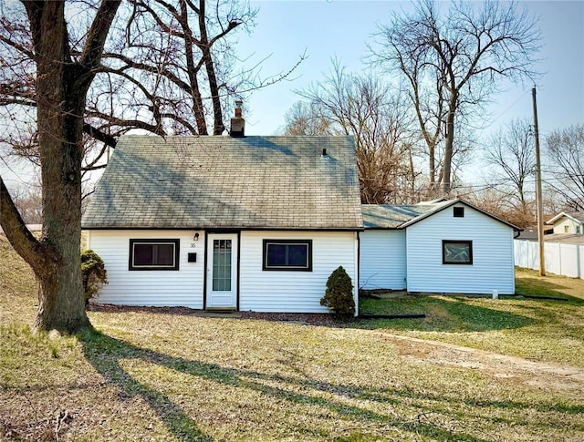 view of front of home with a front yard, fence, roof with shingles, and a chimney