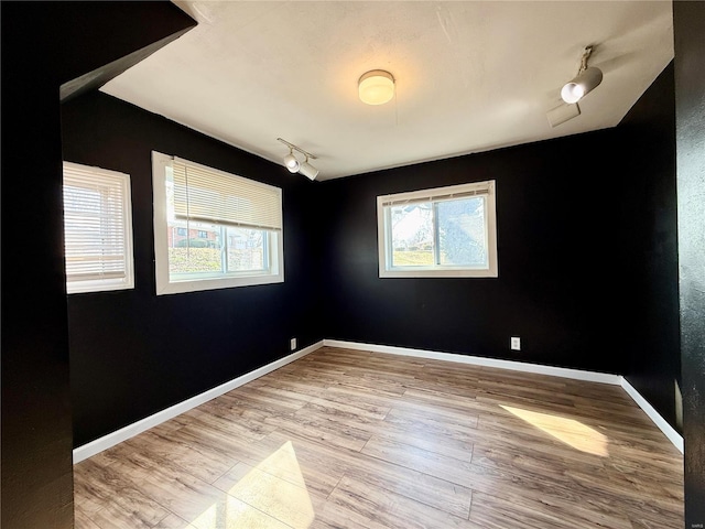 empty room with baseboards, wood finished floors, and rail lighting