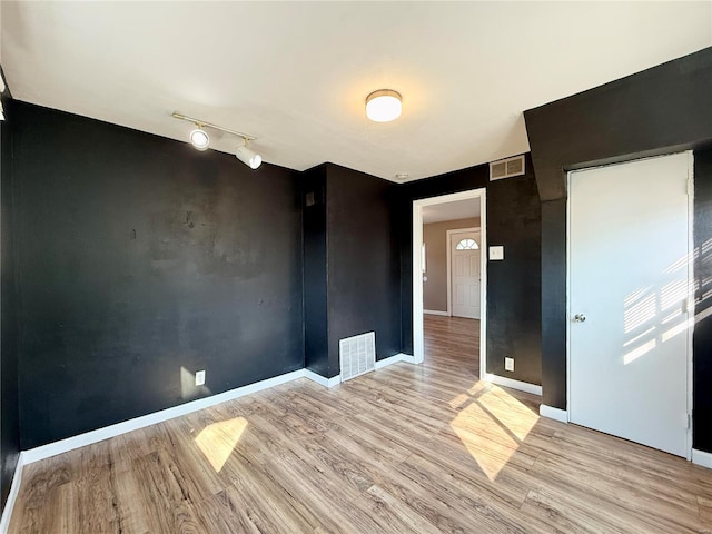 empty room featuring visible vents, rail lighting, baseboards, and wood finished floors