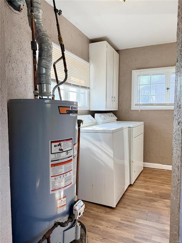 clothes washing area featuring washer and dryer, gas water heater, cabinet space, light wood finished floors, and a textured wall