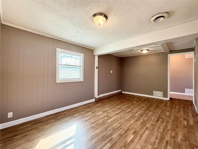 spare room featuring a textured ceiling, wood finished floors, visible vents, and baseboards