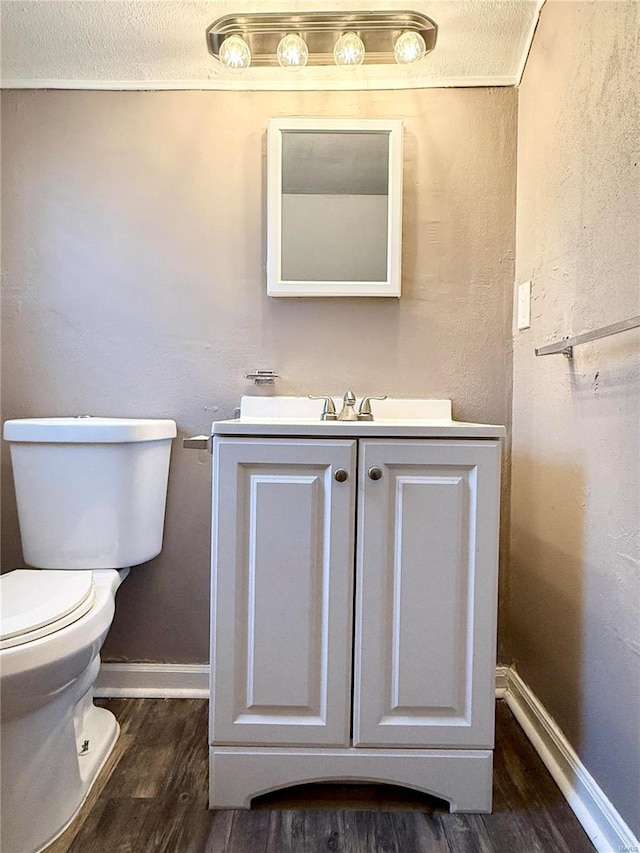 half bathroom featuring toilet, vanity, baseboards, and wood finished floors