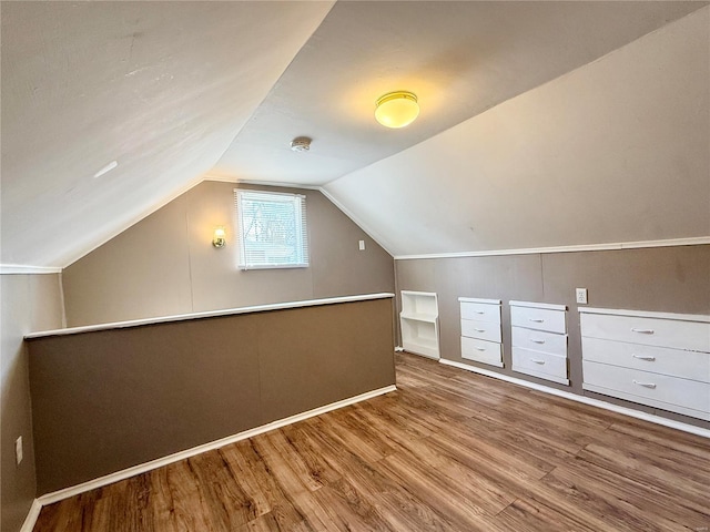 additional living space with baseboards, wood finished floors, and vaulted ceiling