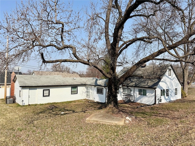 rear view of house featuring a lawn and roof with shingles