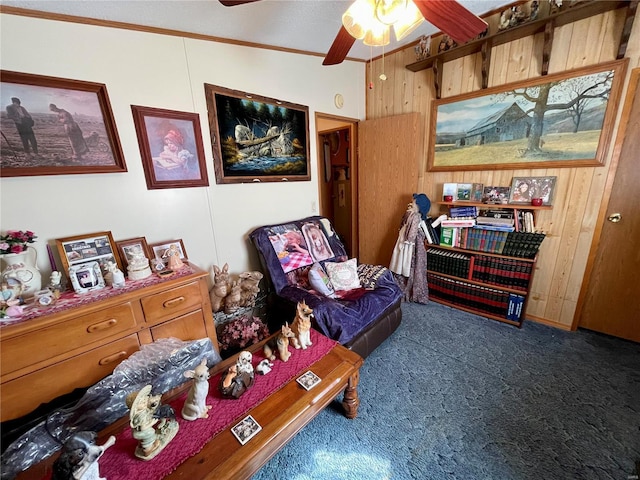 sitting room with wooden walls, carpet flooring, a ceiling fan, and ornamental molding