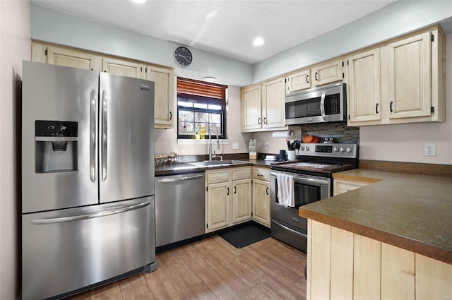 kitchen with a sink, stainless steel appliances, dark countertops, and light brown cabinets