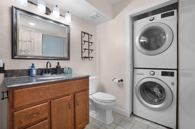 full bathroom with tile patterned floors, visible vents, toilet, stacked washer and clothes dryer, and vanity