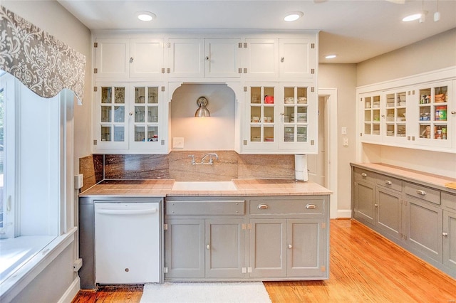 kitchen featuring gray cabinetry, a sink, light wood-style floors, white dishwasher, and light countertops