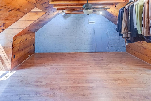 bonus room featuring wooden walls, wood finished floors, visible vents, vaulted ceiling with beams, and ceiling fan