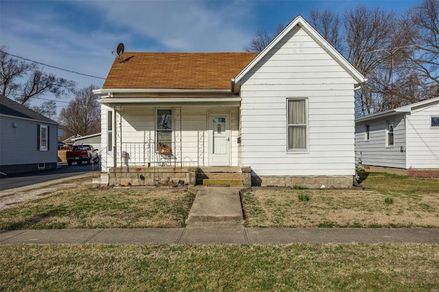 bungalow-style house featuring covered porch, a front yard, and a shingled roof