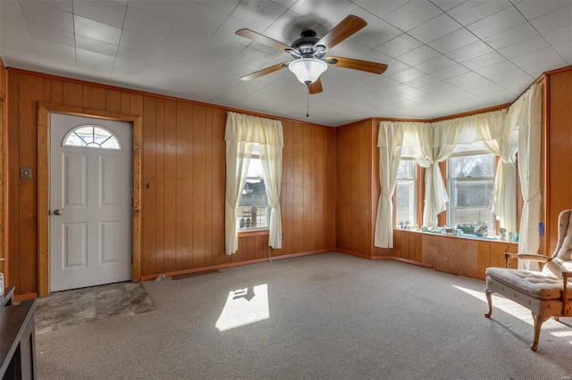 foyer entrance with wood walls, crown molding, ceiling fan, and carpet floors