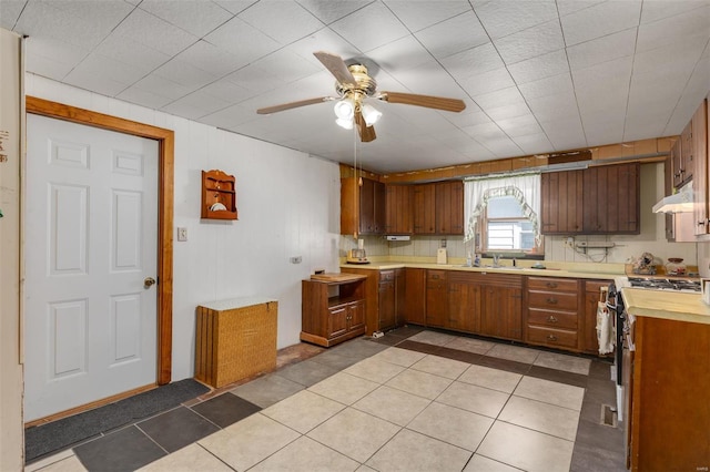 kitchen with under cabinet range hood, light countertops, brown cabinetry, gas stove, and a ceiling fan