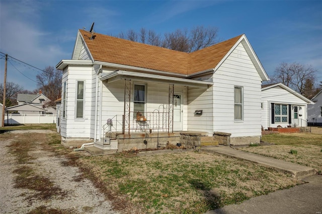 view of front facade with a front lawn, covered porch, and a shingled roof