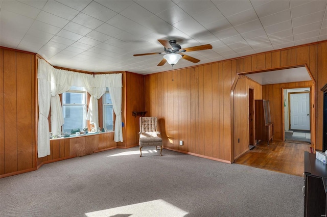 unfurnished room with wooden walls, a ceiling fan, baseboards, and carpet floors