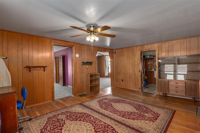 bedroom featuring baseboards, wooden walls, wood finished floors, and a ceiling fan