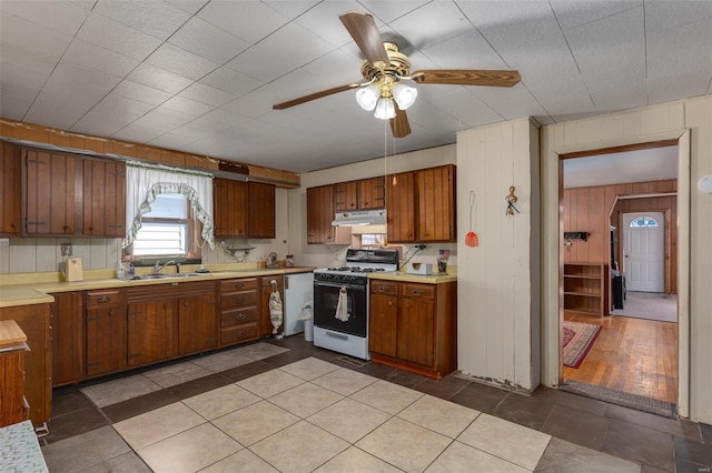 kitchen with dishwashing machine, gas range oven, under cabinet range hood, and light countertops