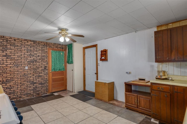 kitchen featuring light tile patterned floors, brick wall, light countertops, and a ceiling fan