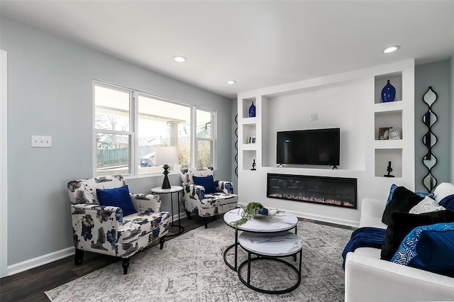 living area featuring built in shelves, a glass covered fireplace, wood finished floors, recessed lighting, and baseboards