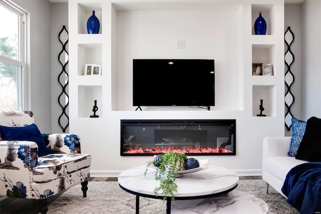 living room with a glass covered fireplace, wood finished floors, and built in features