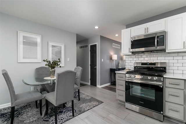 kitchen with decorative backsplash, stainless steel appliances, light countertops, and visible vents