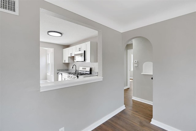 kitchen featuring baseboards, visible vents, dark wood-style flooring, arched walkways, and appliances with stainless steel finishes