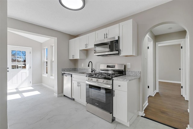 kitchen featuring stainless steel appliances, arched walkways, marble finish floor, white cabinetry, and a sink