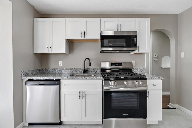 kitchen featuring light stone counters, appliances with stainless steel finishes, arched walkways, marble finish floor, and a sink