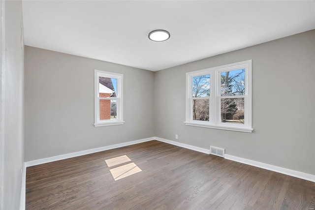 unfurnished room featuring a wealth of natural light, visible vents, dark wood-type flooring, and baseboards