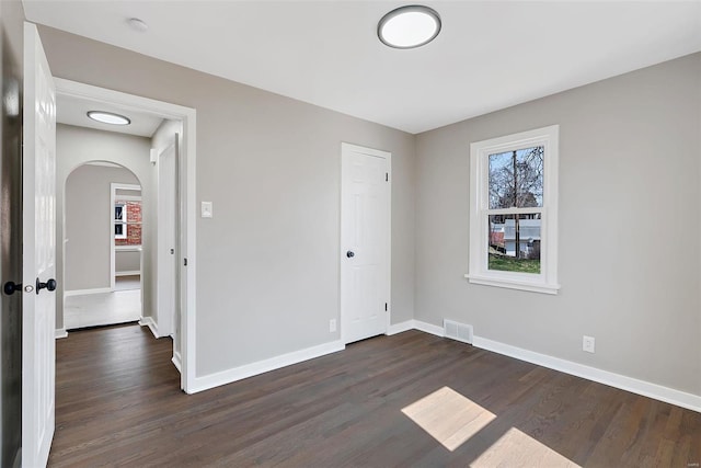 unfurnished bedroom with dark wood-type flooring, visible vents, arched walkways, and baseboards