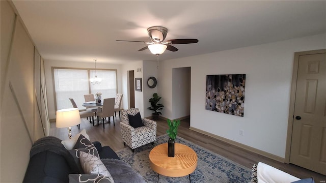 living area featuring wood finished floors, ceiling fan with notable chandelier, and baseboards