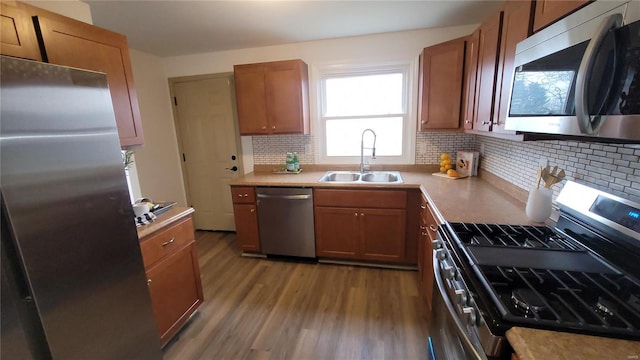 kitchen featuring a sink, backsplash, wood finished floors, stainless steel appliances, and brown cabinetry