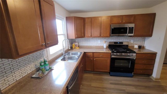 kitchen with tasteful backsplash, brown cabinets, wood finished floors, stainless steel appliances, and a sink