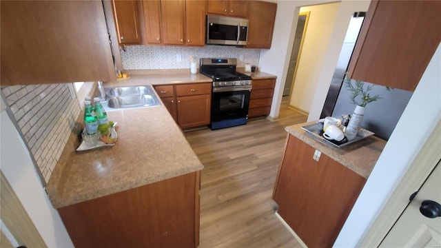 kitchen with decorative backsplash, brown cabinets, appliances with stainless steel finishes, light wood-style flooring, and a sink