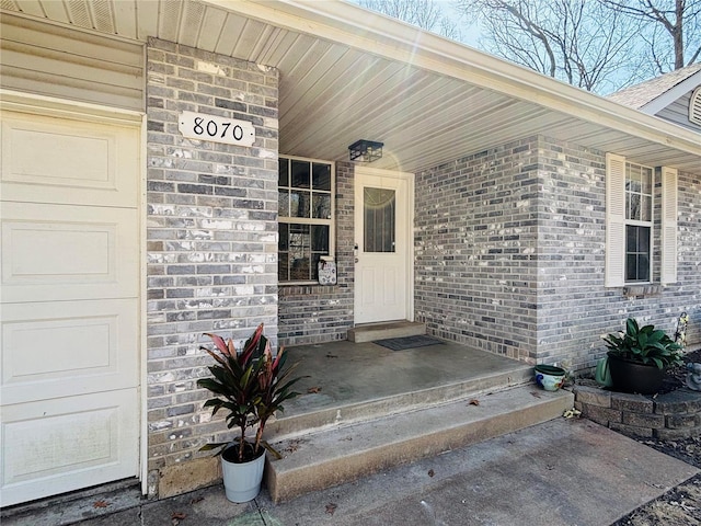 entrance to property with a porch and brick siding