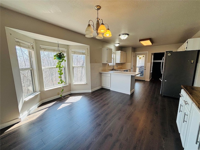 kitchen featuring a peninsula, freestanding refrigerator, an inviting chandelier, dark wood-style floors, and a textured ceiling