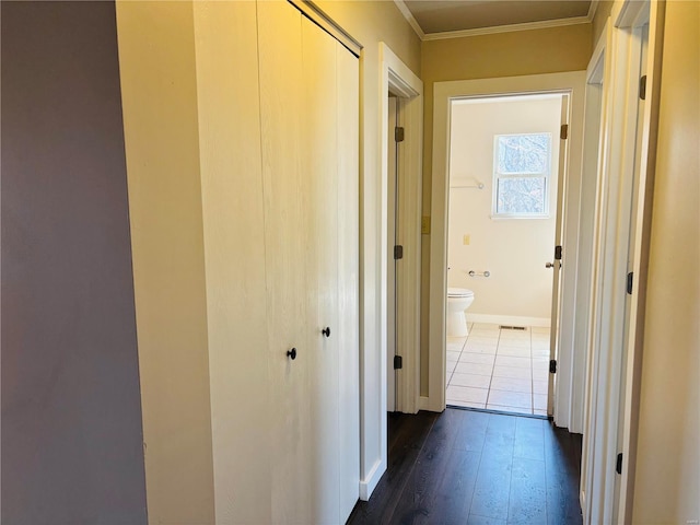 hallway featuring dark wood finished floors, visible vents, crown molding, and baseboards