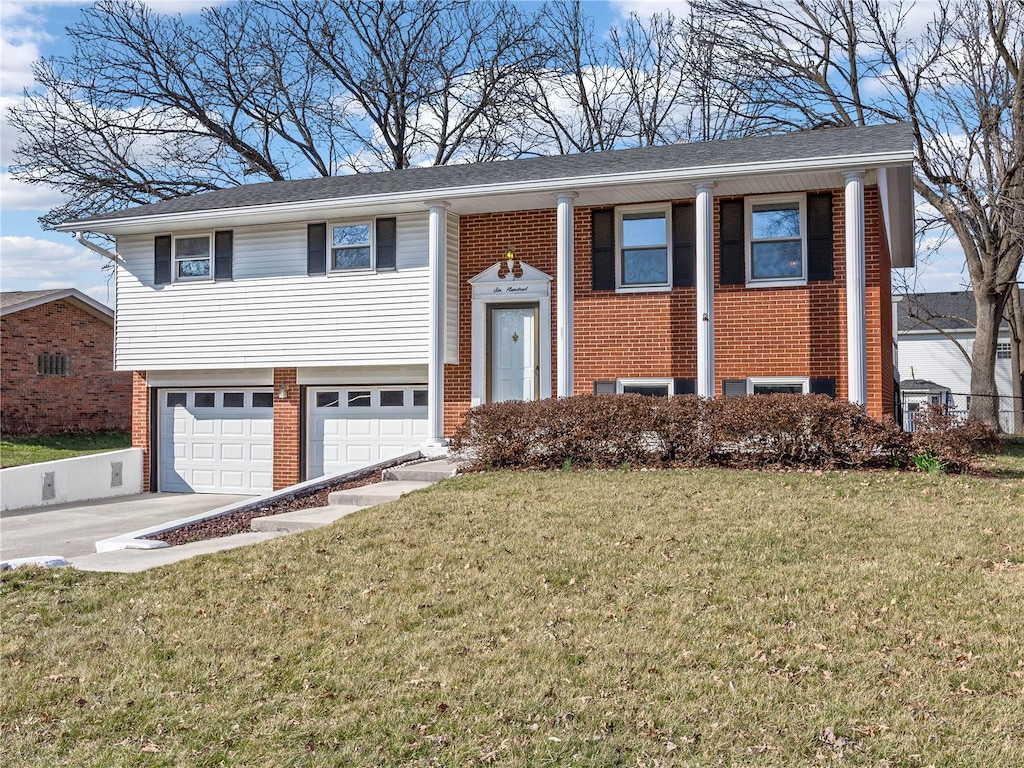 raised ranch with brick siding, a garage, driveway, and a front yard