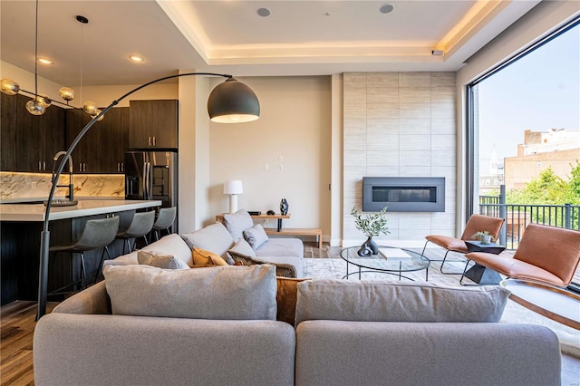 living area featuring recessed lighting, a tile fireplace, a raised ceiling, and wood finished floors