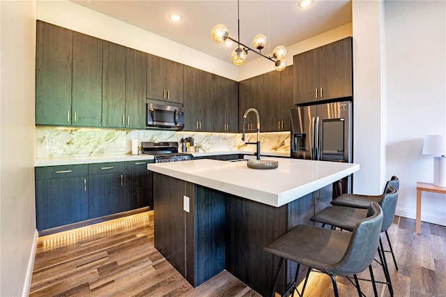 kitchen featuring dark wood-style floors, a sink, appliances with stainless steel finishes, a kitchen bar, and backsplash