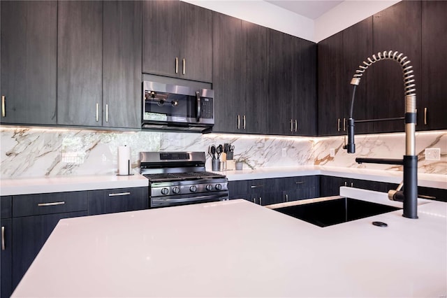 kitchen with a sink, light countertops, dark brown cabinetry, appliances with stainless steel finishes, and backsplash