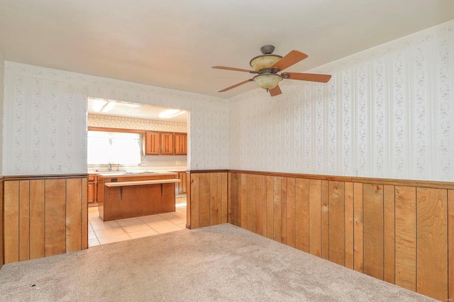 kitchen with a wainscoted wall, light colored carpet, brown cabinetry, and wallpapered walls