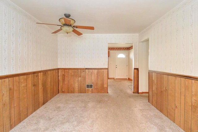 carpeted spare room with visible vents, a wainscoted wall, wallpapered walls, ceiling fan, and wood walls