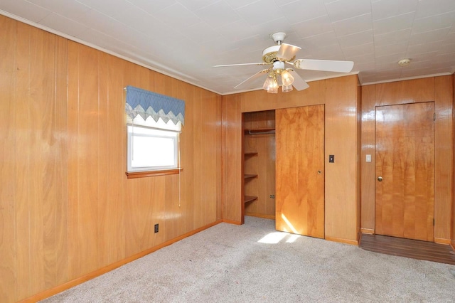 unfurnished bedroom featuring a closet, a ceiling fan, wood walls, and carpet floors