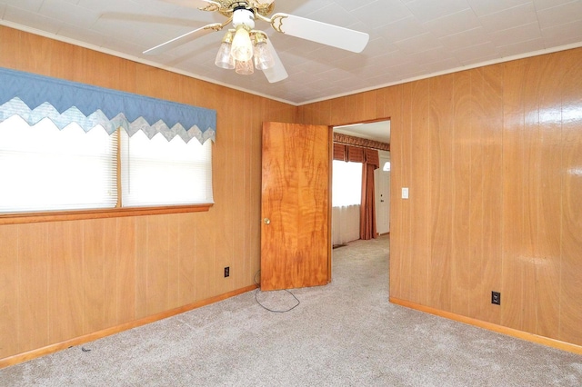 carpeted spare room with crown molding, a ceiling fan, and wood walls