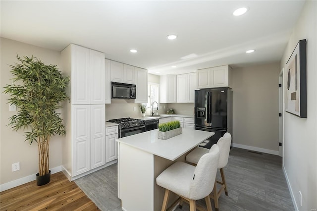 kitchen with black appliances, a breakfast bar, wood finished floors, white cabinets, and light countertops