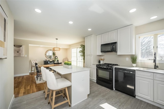 kitchen with a center island, white cabinetry, black appliances, and a sink