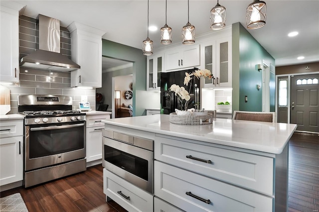 kitchen with appliances with stainless steel finishes, white cabinets, light countertops, and wall chimney range hood