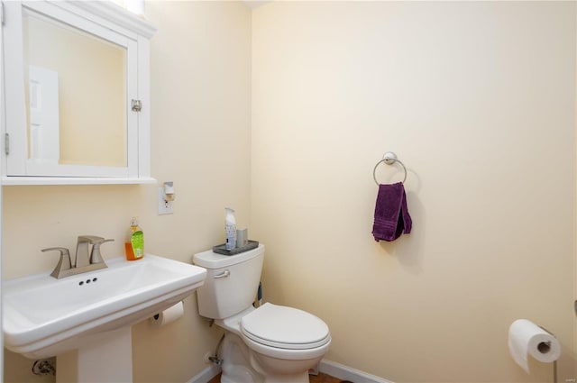 half bath featuring toilet, baseboards, and a sink