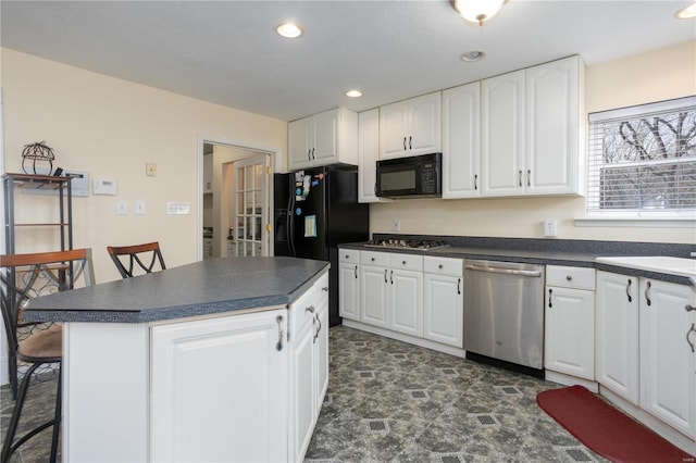 kitchen featuring a kitchen breakfast bar, dark countertops, black appliances, and white cabinetry